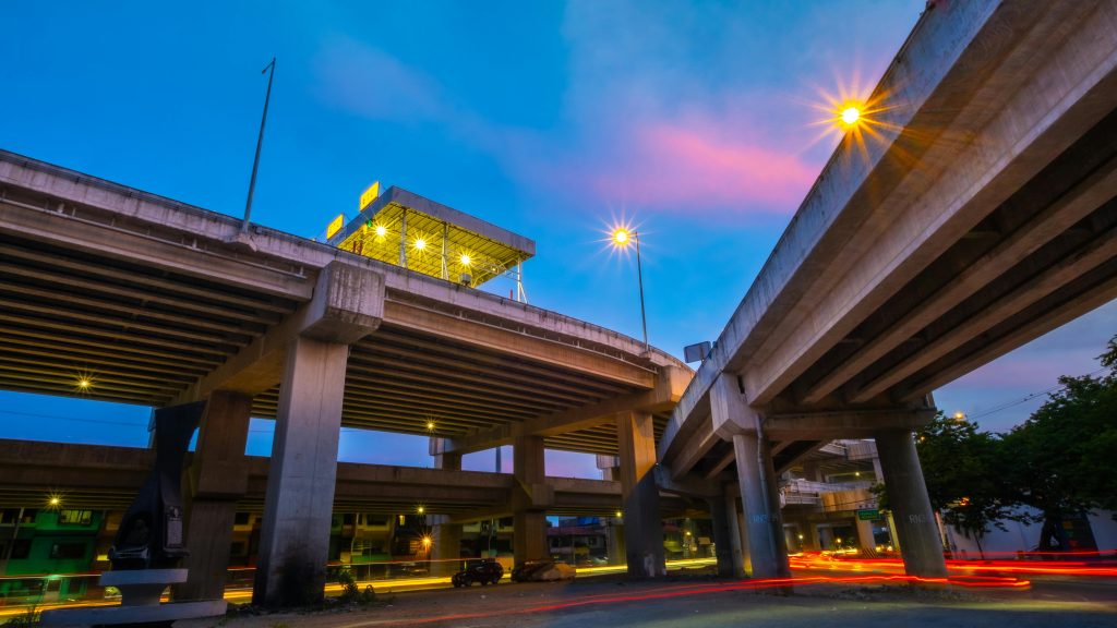A vibrant city highway interchange at twilight with glowing streetlights and car light trails.